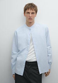 Camicia azzurra chiara con colletto alla coreana, maniche lunghe e vestibilità comoda. Tessuto di cotone texture con bottoni visibili sulla parte anteriore.