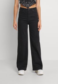 Svarta vida jeans med hög midja, gjorda av denimtyg. Har framfickor och ett metallknäpp. Stylad med en kort topp.