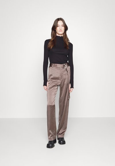 Top negro de manga larga con escote de picos, combinado con pantalones satinados, de talle alto y color topo, que cuentan con un cinturón en la cintura. Botas gruesas negras.