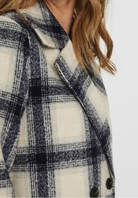 Beige og marineblå plaid uldfrakke med notched krave, dobbeltknapper og struktureret stof. Har store ternede mønstre.