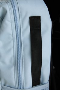 Light blue fabric backpack with a smooth surface, featuring a black woven strap and a visible blue zipper along one side.