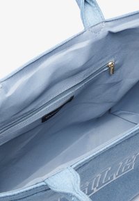Lys blå denim tote taske med to håndtag, lynlås indvendig lomme og stofforing. Har prægede logo på forsiden.