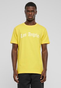 Dzeltena kokvilnas T-krekls ar īsām piedurknēm, ar uzrakstu "Los Angeles" baltā, treknā fonētikā uz krūtīm. Standarta piegriezums un apaļa kakla forma.