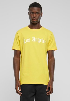 Gul bomull t-skjorte med korte ermer, med teksten "Los Angeles" i hvit, fet skrift over brystet. Standard passform og rund hals.