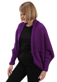 Cardigan morado de punto acanalado con mangas anchas y un frente abierto. Llevado sobre una blusa negra, que presenta un corte holgado y una tela texturizada.