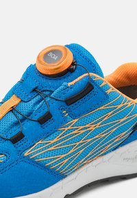 Niebieskie buty sportowe z teksturowaną cholewką, pomarańczowymi akcentami, systemem zapięcia BOA oraz białą i czarną bieżnią.