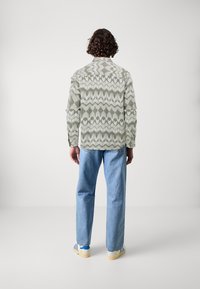Lichtgroen, gemusterd shirt met een kraag, lange mouwen en een losse pasvorm, gecombineerd met blauwe jeans en casual schoenen met blauwe strepen.