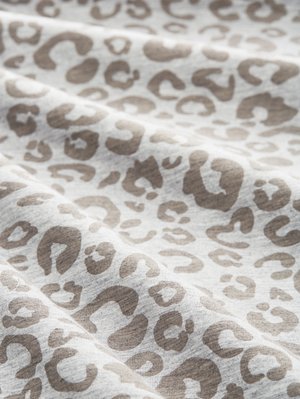 Läheltä kuvattu pehmeä kangas, jossa on vaaleanharmaa ja beige leopardikuosi sekä hellät laskokset.
