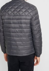 Giubbotto puffer trapuntato grigio con cuciture orizzontali, colletto alto e polsini elasticizzati. Tessuto liscio e lucido con un design leggero.