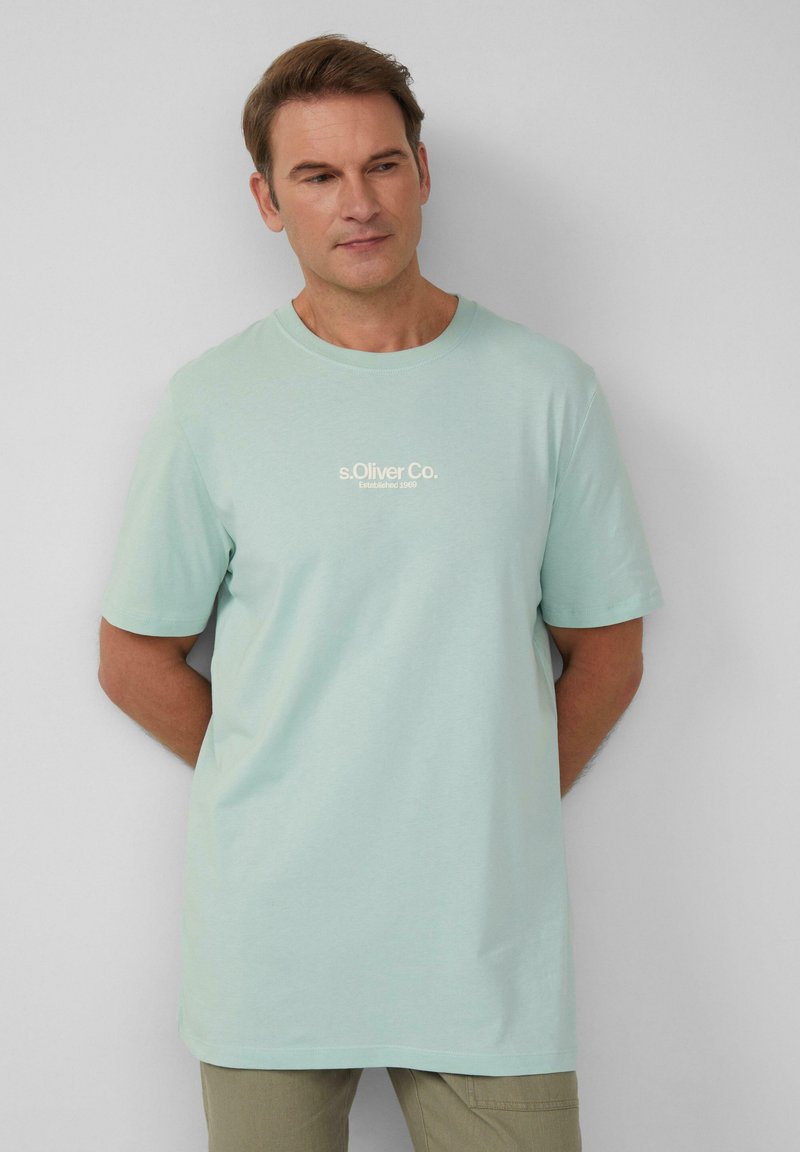 Licht mintgroene katoenen t-shirt met korte mouwen, ronde halslijn en opdruk met witte logo tekst aan de voorkant. Stevige textuur, ontspannen pasvorm.