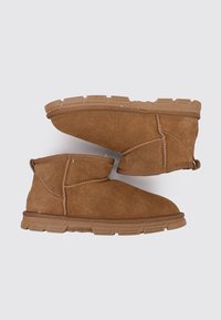 Braune Wildleder-Ankle-Boots mit runder Zehe, weicher Textur, kontrastierenden Nähten und einer dicken Gummisohle mit strukturierten Grip-Mustern.