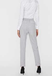 Pantalons gris clair texturé avec une taille élastique et des manches roulées, assortis à une chemise blanche à manches longues et des escarpins noirs.