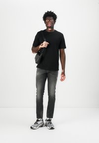T-shirt noir à manches courtes, jean gris déchiré et chaussures de sport noir et blanc. Sac bandoulière noir porté en diagonale sur le corps.