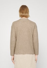 Pull en tricot beige avec un motif texturé, col rond et manches longues, présentant un ourlet droit et une coupe décontractée.