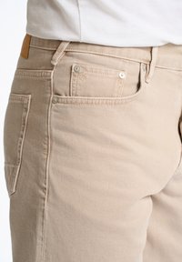 Beige denim broek met een slim fit, voor- en achterzakken en zilverkleurige hardware. Textuurstof met subtiele stikdetails.