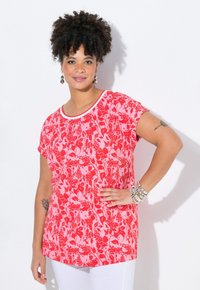 Top de manga corta con un estampado de flores rojas sobre un fondo rosa, con un escote blanco y un corte relajado, hecho de una tela suave.