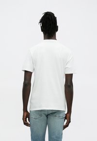 Biała koszulka z krótkim rękawem wykonana z bawełny, z okrągłym dekoltem i luźnym krojem. Noszona z jasnoniebieskimi dżinsami.