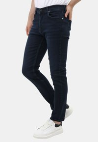 Donkerblauwe slim-fit jeans met vijf zakken, een knoopsluiting en subtiele whiskering aan de voorkant voor extra textuur.