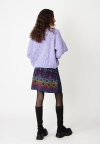 Pull en maille lavande avec des motifs en diamant texturés, associé à une jupe à motifs multicolores. Des bottes noires jusqu'au genou complètent le look.