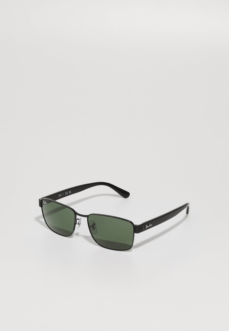 Musta ristkülikukujuline päikeseprillid roheliste läätsedega, metallaktsendid raamidel ja allkiri logo tempelitel. Kerge ja õhuke disain.