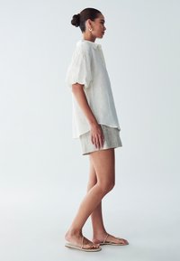 Witte linnen blouse met pofmouwen, lichtbeige linnen shorts en beige sandaaltjes met bandjes. Minimalistisch ontwerp op een neutrale achtergrond.