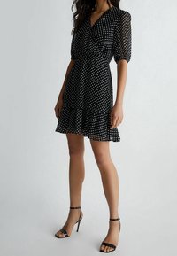 Musta pilkkukuviollinen mekko, jossa on lyhyet puffimaiset hihat, V-pääntie ja laakeat helmat. Yhdistetty mustiin remmikenkiin. Kevyt ja tekstuurinen kangas.