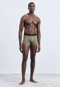 Olivenfargede boxerbokser laget av myk stoff, med en svart linning med "HUGO" logo. Glatt tekstur og tettsittende fasong.