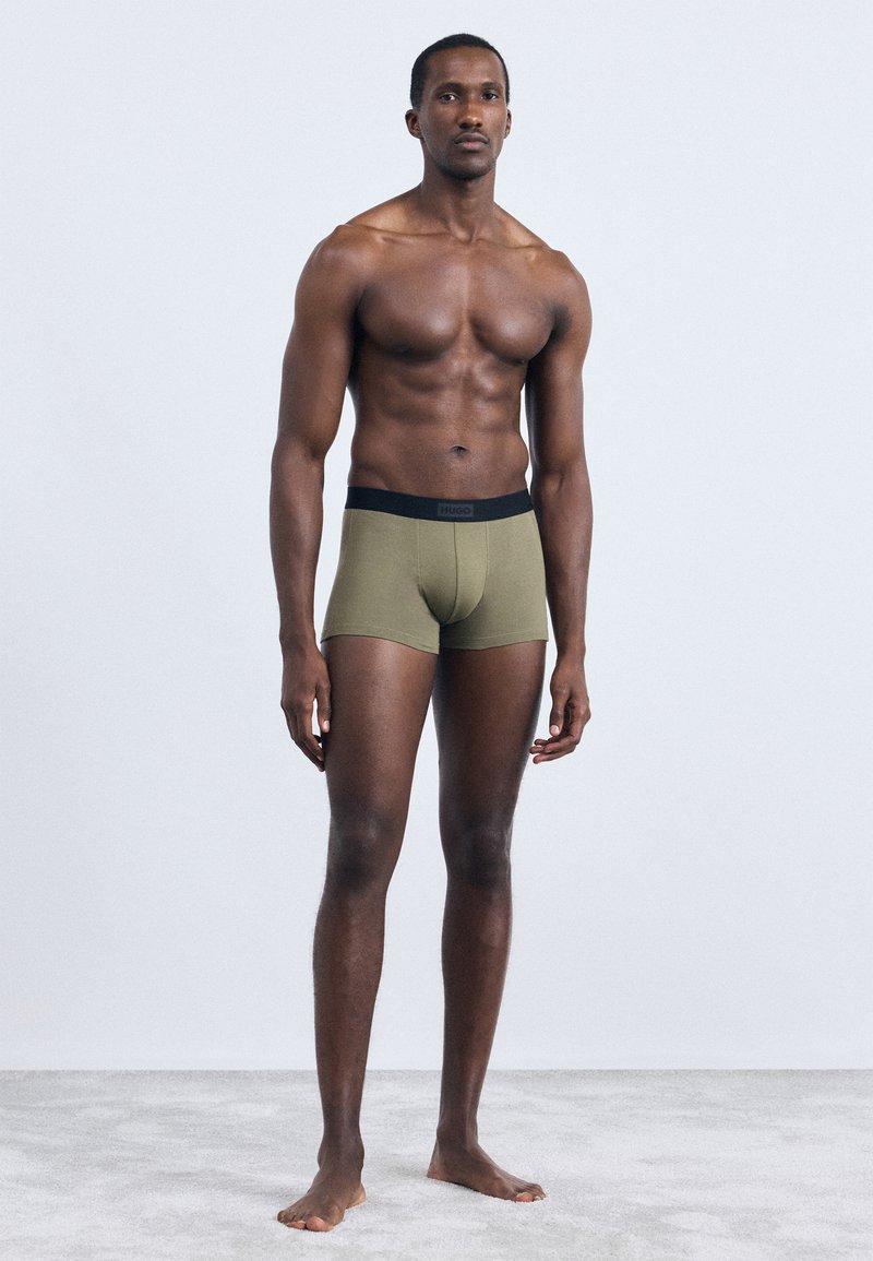 Olivenfargede boxerbokser laget av myk stoff, med en svart linning med "HUGO" logo. Glatt tekstur og tettsittende fasong.