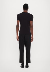 Tricou negru cu mânecă scurtă și guler rotund, asortat cu pantaloni negru tapered și pantofi din piele negri, văzut din spate.
