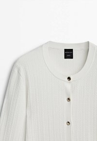Cardigan blanc en maille avec encolure ronde et trois boutons métalliques sur le devant, étiqueté Massimo Dutti Studio.