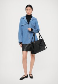 Jeanshemd mit zwei Brusttaschen, schwarzer Rollkragenpullover, schwarzer Lederrock und flachen Schuhen. Große schwarze Tasche mit Faltendetail.