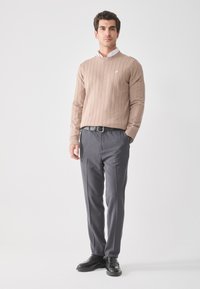 Pull en beige à côtes avec des manches longues, associé à un pantalon de costume gris et des chaussures noires. Chemise blanche à col visible en dessous.