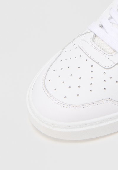 Fehér bőr sneaker perforált dizájnnal, lapos fehér fűzőkkel és texturált gumitalppal, finom varrási részletekkel.