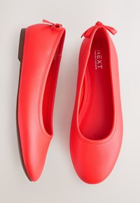 Paar rote Ballerinas mit abgerundeten Zehen und kleinen gebundenen Schleifen vor neutralem Hintergrund, mit Ansichten von oben und von der Seite.