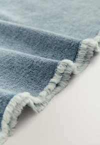 Denim tkanina u svijetloplavoj boji, s poderanim rubovima i teksturiranom površinom, naglašavajući ležeran, neuredan dizajn.