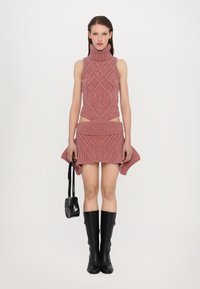 Completo a due pezzi lavorato a maglia di colore rosa con colletto alto, caratterizzato da motivi testurizzati, lati aperti e una gonna svasata. Abbinato a stivali neri sopra il ginocchio.