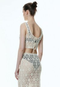 Gehaakte crop top en bijpassende rok in het wit, met bloemenpatronen en hexagonale ontwerpen. Textuur met open weving toont de huid eronder.
