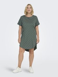 Grön klänning med polka prickar, korta ärmar, avslappnad passform och rundad fåll. Bärs med vita sneakers som har en mjuk, slät textur.