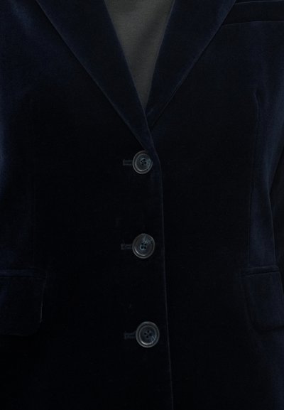 Blazer in velluto blu navy con bavero con risvolto a incavo, quattro bottoni frontali, tasche laterali e una texture liscia. Design semplice e classico.
