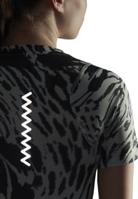 Nærbillede af en persons øvre ryg iført en sort og grå mønstret skjorte med et vertikalt hvidt zigzag-design nær rygsøjlen.