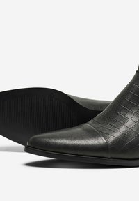 Botas de cuero negro hasta el tobillo con un patrón texturizado de cocodrilo, punta afilada y una puntera lisa. Cuenta con una suela elegante y duradera con un dibujo mínimo.