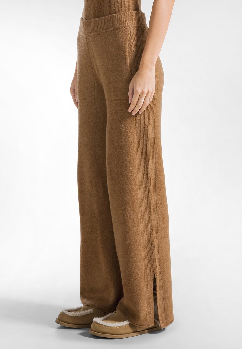 Pantalones de pierna ancha marrones, hechos de un material de punto suave, con acentos de canalé vertical y bolsillos laterales, y aberturas en el dobladillo.