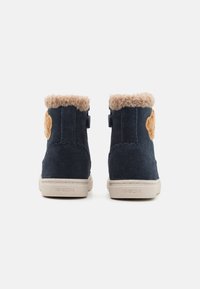 Stivali alla caviglia in suede blu navy con un risvolto in pelliccia sintetica beige, dettagli ondulati e suola in gomma beige. Logo del brand sul retro.