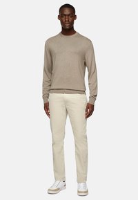 Light beige crewneck sweater in a textured knit, paired with off-white chinos and white sneakers with beige accents.