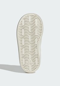 Suola della scarpa con un motivo ondulato, realizzata in gomma cremoso testurizzata. Presenta il logo Adidas al centro. Bordi lisci e forma arrotondata.