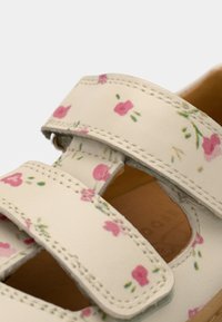 Άσπρο σανδάλι με λουλουδάτο μοτίβο και δύο ρυθμιζόμενους ιμάντες. Διακοσμημένο με ροζ λουλούδια και πράσινα φύλλα σε υφή υλικού. Καφέ σόλα.