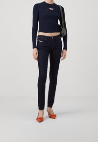 Mörkblå ribbad croptop med logotyp, mörkblå smala jeans och orange höga klackskor. Minimalistisk handväska med blank finish.