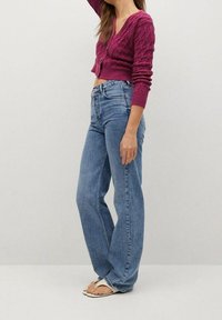 Cardigan magenta lavorato all'uncinetto con scollatura a V e bottoni, abbinato a jeans in denim blu a vita alta, con gamba dritta e lavaggio chiaro.