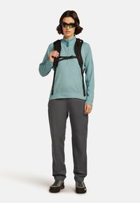 Lichtblauwe lange mouw pullover met een kwart rits, gecombineerd met donkergrijze broek en zwarte wandelschoenen. Bevat een zwarte rugzak harnas.