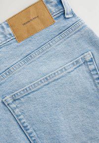 Lichtblauwe denim jeans met een tan leren label met de tekst "DENIM SUPPLY," voorzien van een klassieke snit en zichtbare stikseldetails.